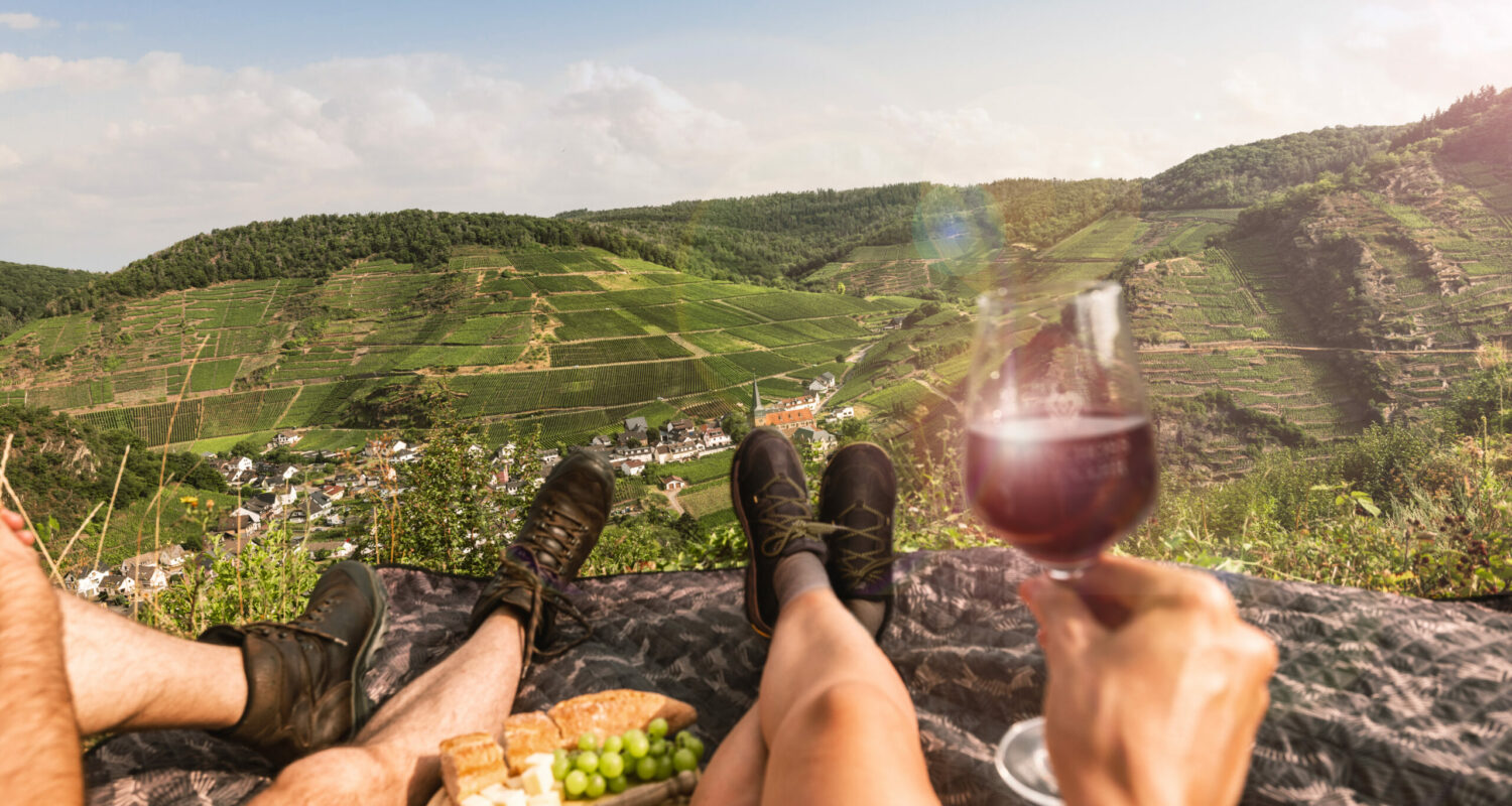 Weingenuss mit Panorama an der Saffenburg im Ahrtal (POV) Nach dem Aufstieg zur Saffenburg, der größten Höhenburg der Region, eröffnet sich ein faszinierender Ausblick auf den Weinort Mayschoß und die umliegenden Weinberge – der perfekte Moment zum Innehalten inmitten der Natur mit dem Duft des Sommertages in der Nase und dem Geschmack eines köstlichen Spätburgunders auf der Zunge.