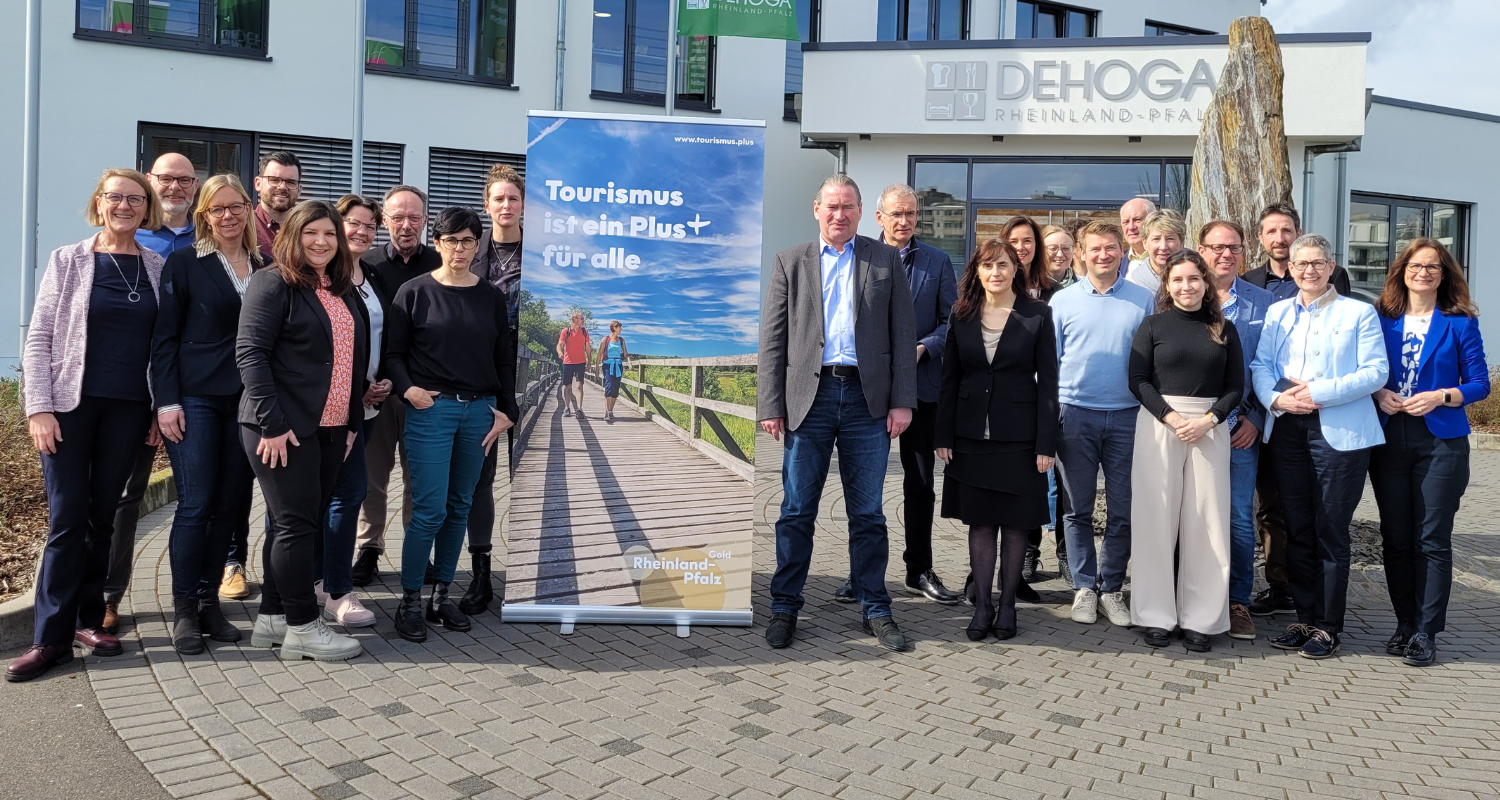 Tourismus ist ein Plus für alle, davon sind die Partner im Tourismus in RLP überzeugt. Eine Gruppe von Personen - Partner im Tourismus - steht vor dem DEHOGA-Gebäude. In der Mitte der Gruppe steht ein Banner mir der Aufschrift :"Tourismus ist ein Plus für Alle"