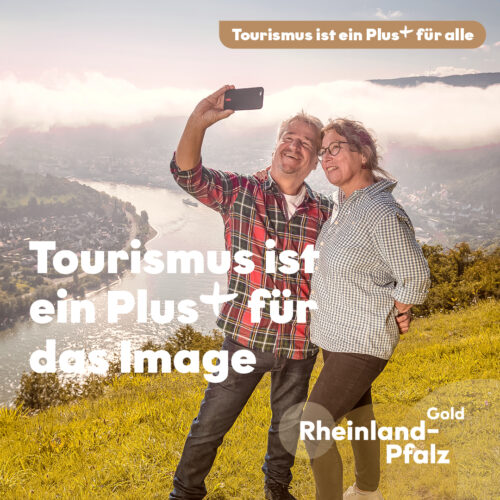 Tourismus Plus fürs Image_quadratisch Kampagnenmotiv zum Thema Tourismus ist ein Plus für das Image: Zwei Personen machen auf einem Aussichtspunkt ein Selfie mit Blick auf eine Flusslandschaft.