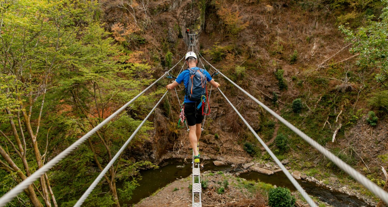 Hängeseilbrücke auf dem Burgenklettersteig Abenteuerlustige und Naturfreunde, die das besondere Klettererlebnis abseits der Alpen suchen, sind auf dem Manderscheider Burgenklettersteig richtig. Das malerische Tal der Lieser und die beiden Manderscheider Burgen bilden die Kulisse für den mit dem Tourismuspreis Rheinland-Pfalz als „Innovation des Jahres“ ausgezeichneten Klettersteig. In drei Etappen mit verschiedenen Schwierigkeitsgraden schlängelt sich der Steig entlang der zerklüfteten Felsen des Liesertals und rund um die Manderscheider Burgen. Jede Etappe wartet mit eigenen Herausforderungen und Höhepunkten auf, von steilen Kletterpassagen bis zu Hängebrücken, die Adrenalinschübe garantieren. Besonders die 20 Meter hohe und 60 Meter lange Hängeseilbrücke, die kurz vor dem Gipfelkreuz überquert wird, ist nichts für Angsthasen.